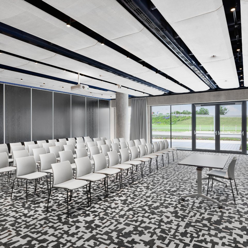 White conference chairs facing a presentation area by the windows.