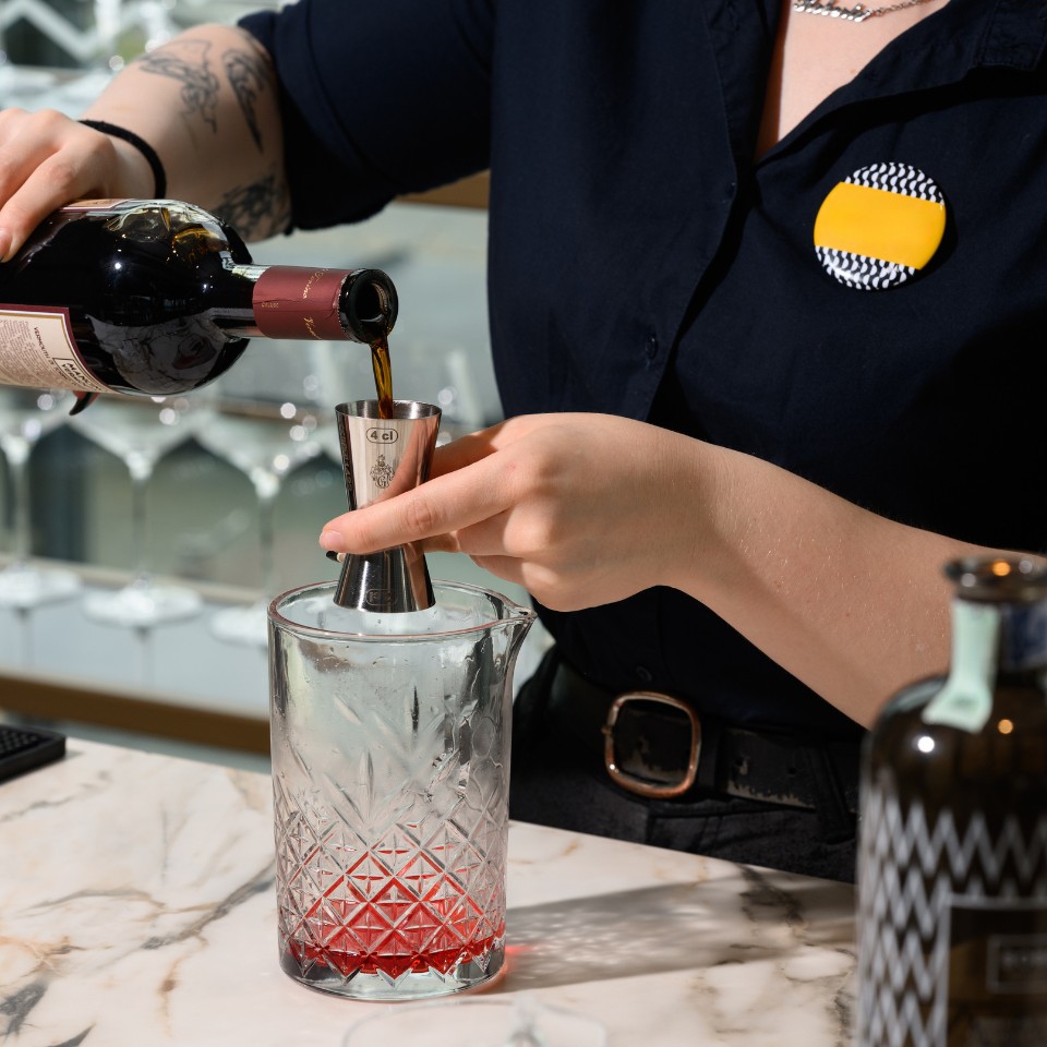 A bartender measures a drink above a mixing glass.