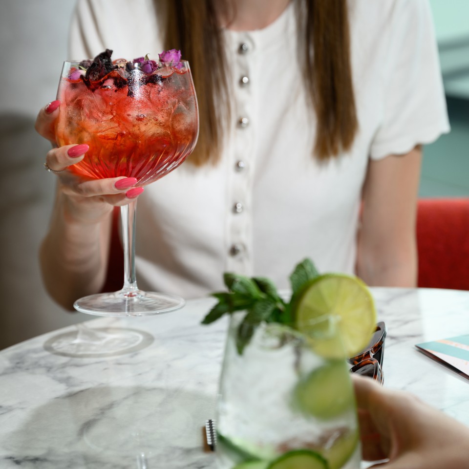 Guests holding red and green cocktails at a marble table.