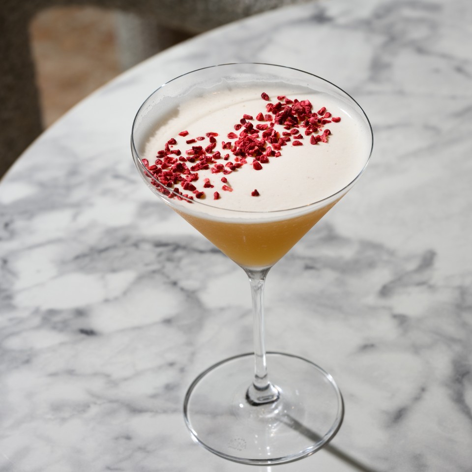 Cocktail with a foamy white top and red garnish.