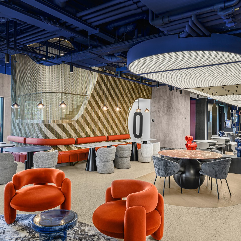Modern interior with orange and gray seating, a zigzag wall pattern, and artistic lighting. A round light fixture creates a contemporary ambiance.