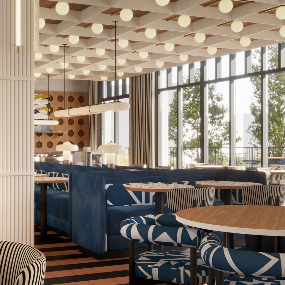 Living area with blue upholstered booth seating, round wooden tables, patterned armchairs, large windows, and a ceiling with a grid of round lights
