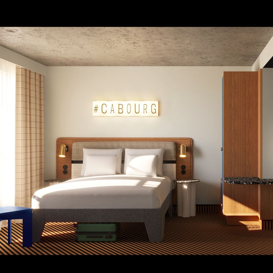 Modern hotel room with a double bed, two pillows, bedside lamps, a blue stool, and a lighted #CABOURG sign on the wall.