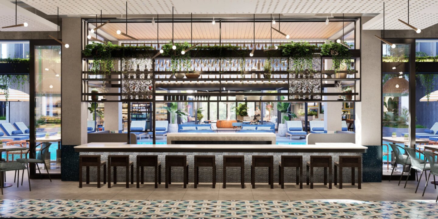 Stylish hotel bar counter with dark wood stools looking out toward a sunny outdoor pool deck and lounge area.