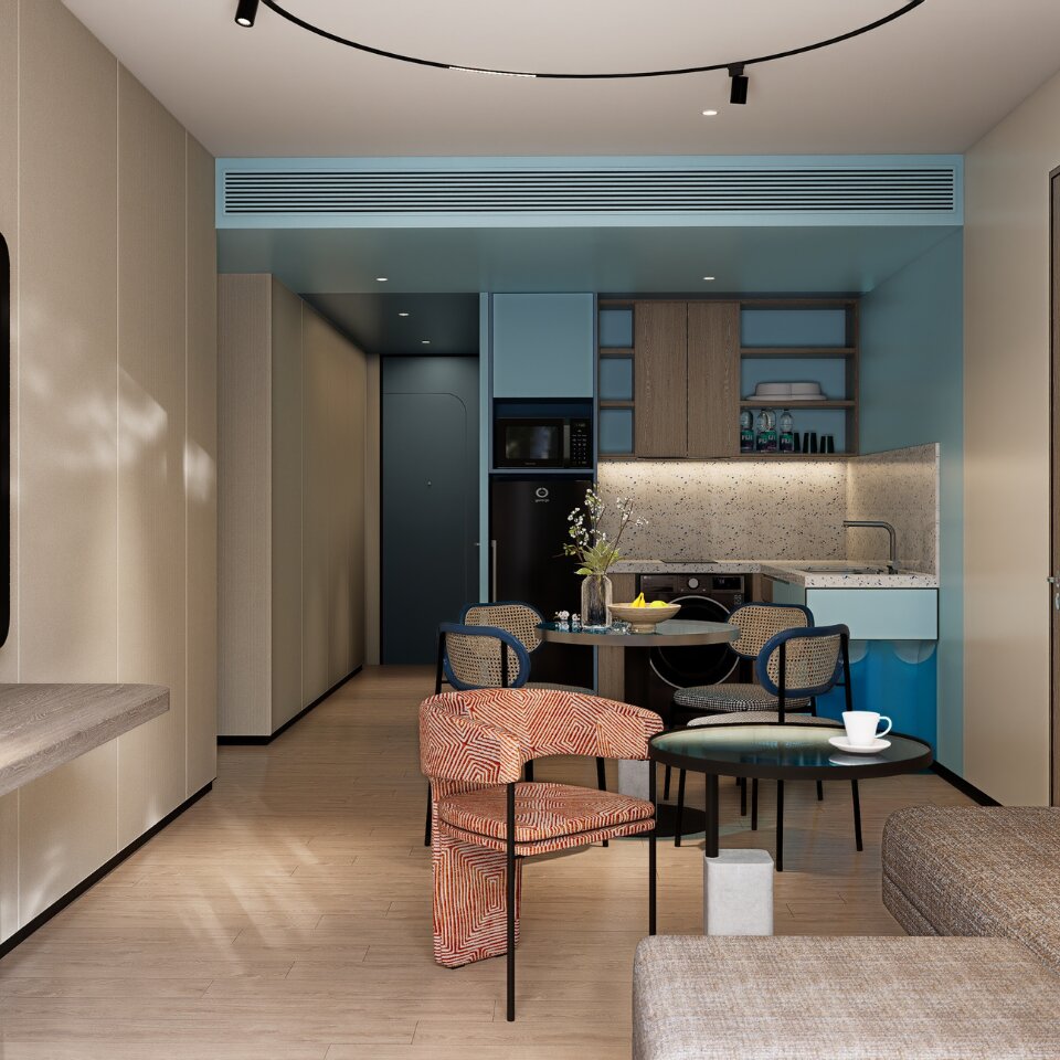 Modern hotel suite interior featuring a compact kitchenette, dining table with woven chairs, a stylish orange patterned armchair, and a cozy living area.
