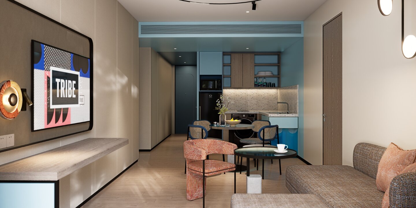 Modern hotel suite interior featuring a compact kitchenette, dining table with woven chairs, a stylish orange patterned armchair, and a cozy living area.