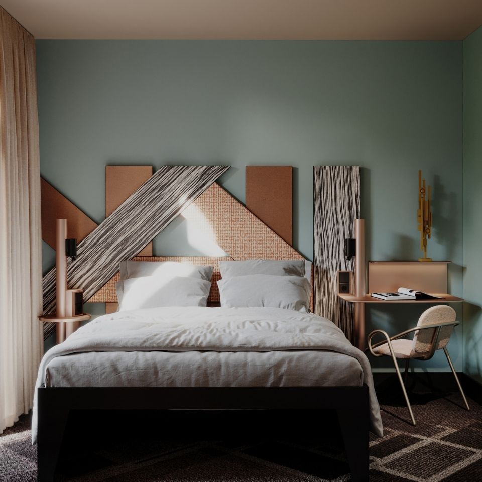 Stylish hotel guest room featuring a double bed with a custom geometric headboard made of wood and patterned fabric panels against a sage green wall.