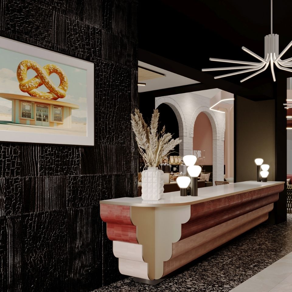 Modern hotel lobby reception counter with a tiered terracotta-and-gold design, set against a textured black wall featuring a framed photograph of a giant pretzel.