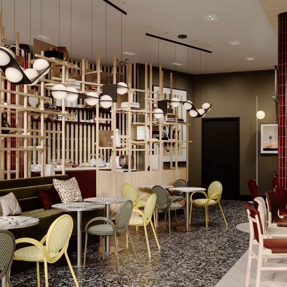 Modern hotel café and bistro area featuring round marble tables, patterned yellow and green chairs, terrazzo tile flooring, and a light-wood lattice room divider with globe pendant lights.
