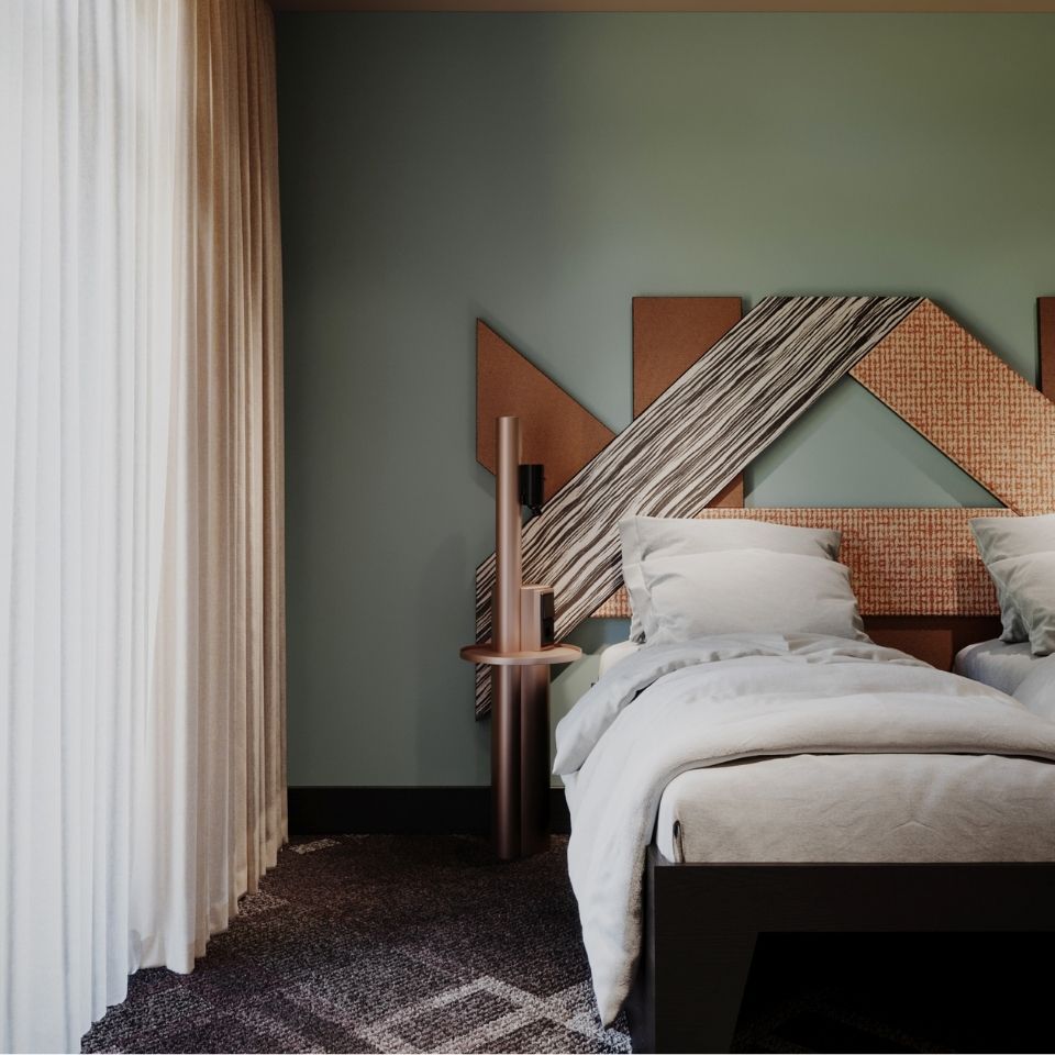 In-room hotel beverage station and workspace with a rose-gold shelving unit, coffee maker, a patterned vanity stool, and a wall-mounted TV with TRIBE on screen.