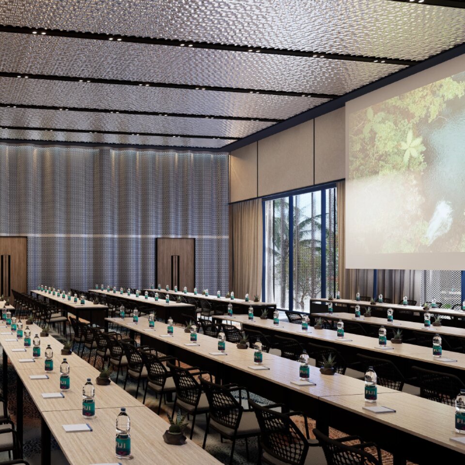 Spacious seminar hall arranged in classroom format featuring rows of long tables, black mesh chairs, and a large projection screen displaying a nature scene.