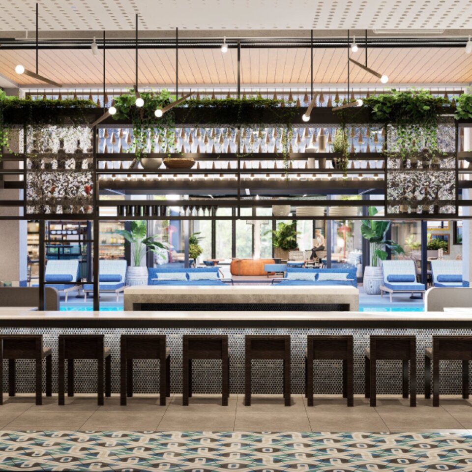 Stylish hotel bar counter with dark wood stools looking out toward a sunny outdoor pool deck and lounge area.