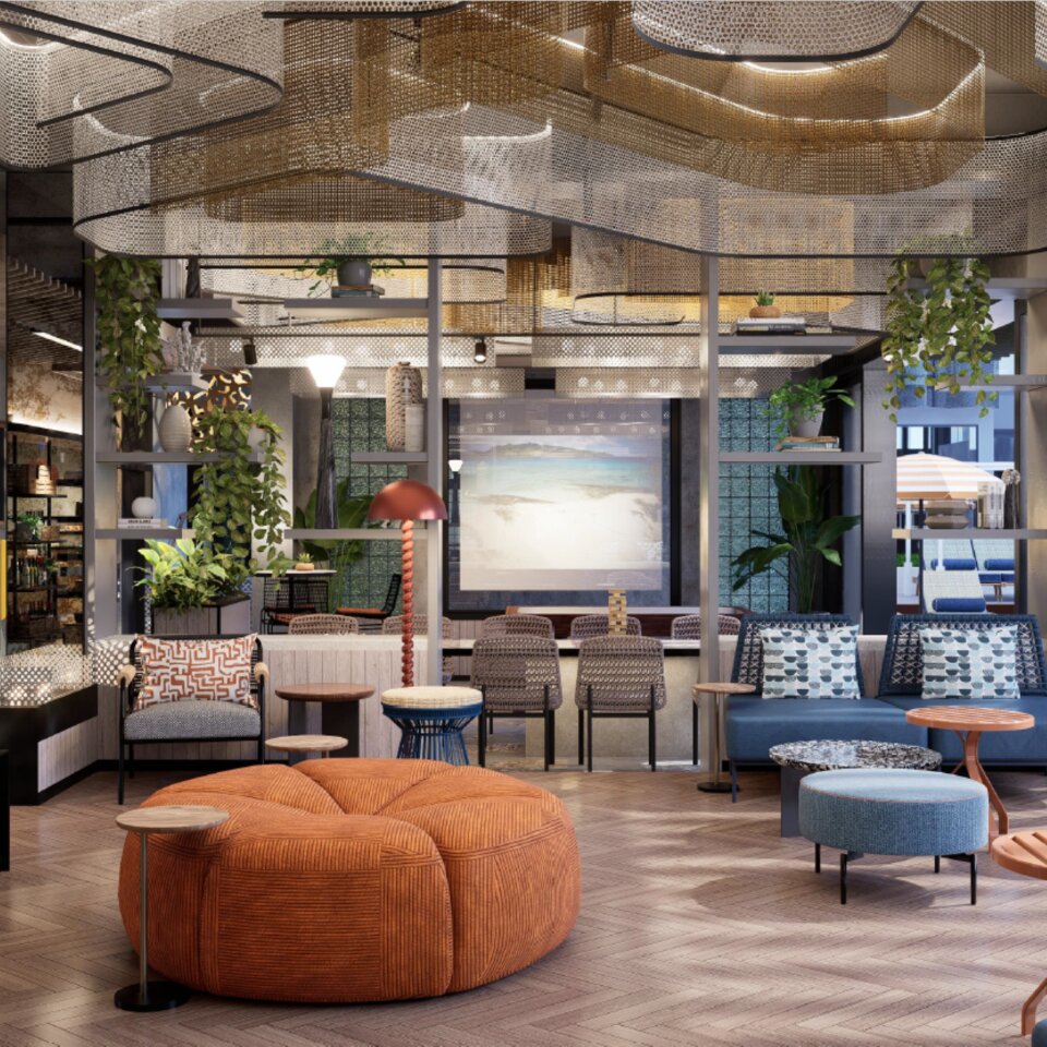 Trendy hotel lobby lounge featuring a large orange round pouf, blue sofas, geometric wooden floors, and hanging mesh ceiling installations.